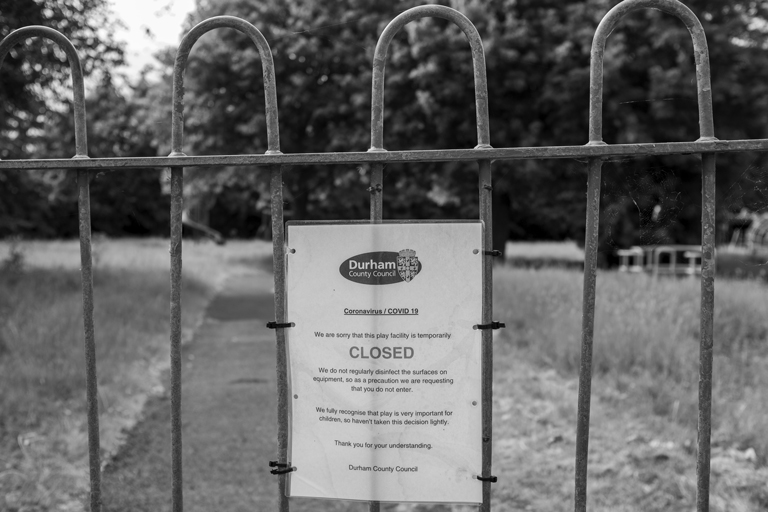 A closed playground in Durham during the COVID-19 pandemic, a closure notice is attached to a locked gate